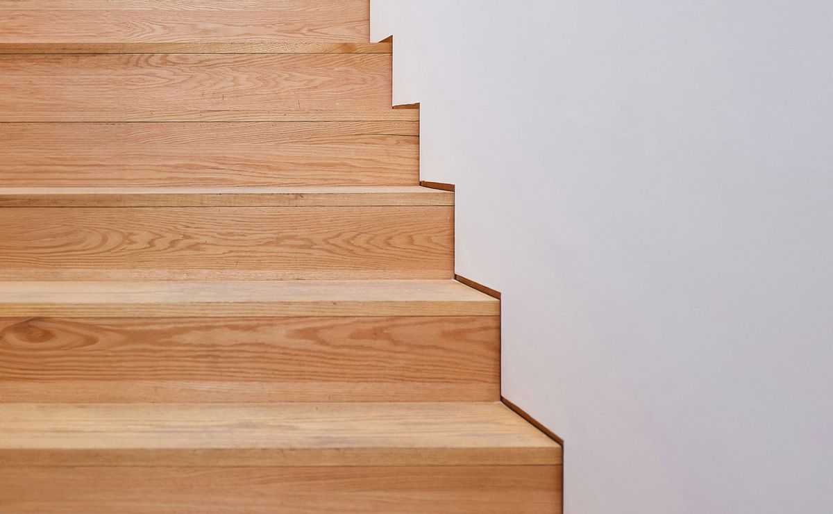 Eine Nahaufnahme einer hellen Holztreppe mit klaren Linien, die vor einer glatten weißen Wand nach oben führt.